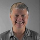 A photo of the owner, Mark Lister, smiling wearing a gray collared polo t-shirt in a silver background.